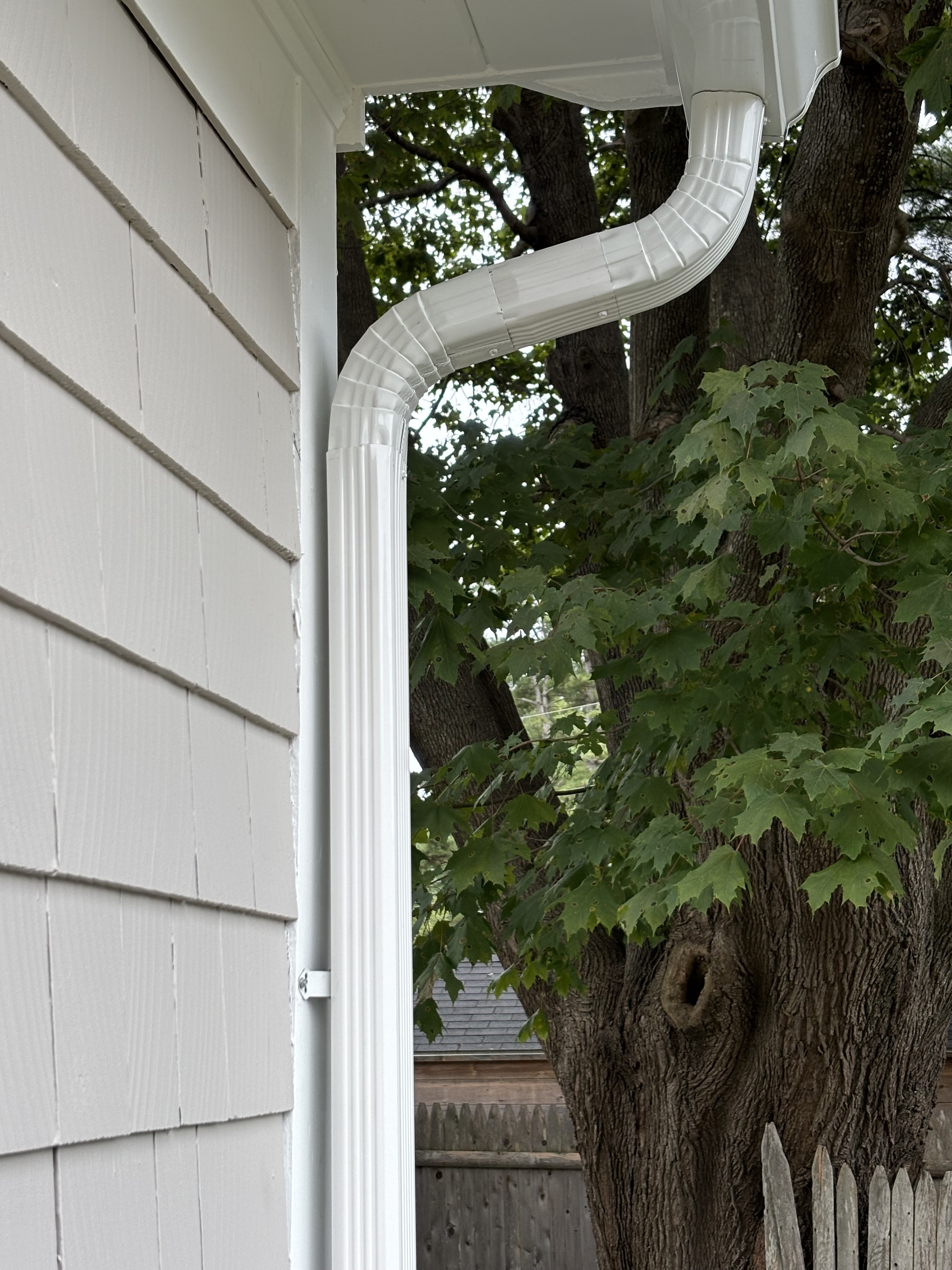 White round downspout with elbow against white painted siding